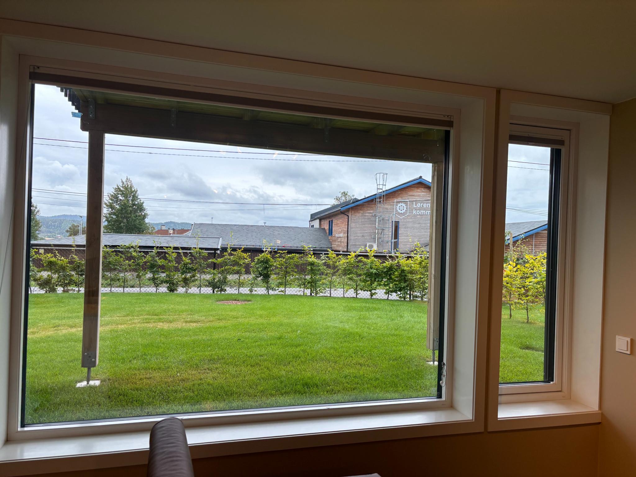 Fint utsyn fra stuevinduet til pent beplantet hage.
Elektrisk, utvendig solskjerming på stuevindu, samt innvendig solskjerming med doble plisségardiner som kan justeres både fra toppen og bunnen.
